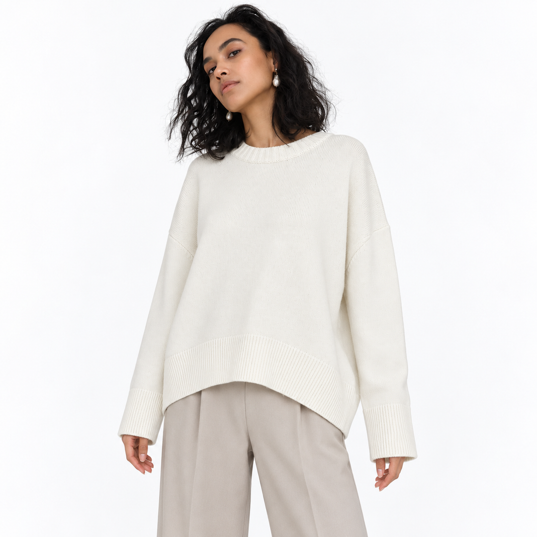 White knitted pullover on a model in a white studio, showing its crew neckline, long sleeves, relaxed shape and ribbed edges.