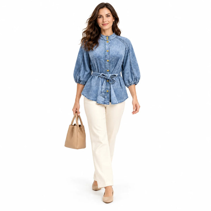 Adult model wearing the belted Washed Blue T0308 blouse with cream trousers and a tan tote handbag in a white studio setting.