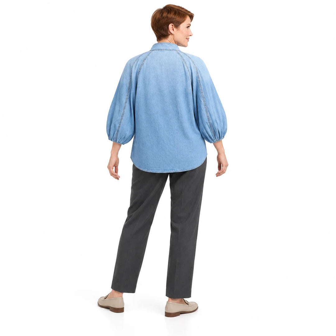 Adult model wearing the Light Blue 1481029 denim blouse from the back, with gathered sleeves and a curved hem on plain white.