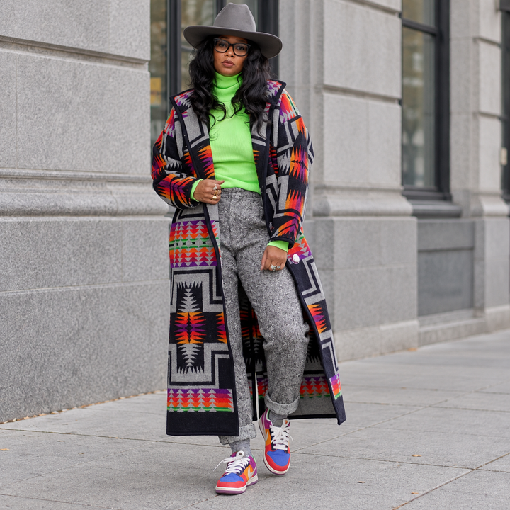 Full-body model walking in the geometric print long coat with a green top and gray trousers.