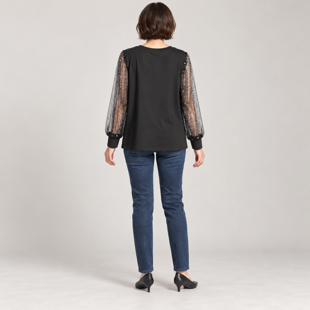 Back view of the black top with a plain back, sheer dotted sleeves and opaque cuffs on a full-length model