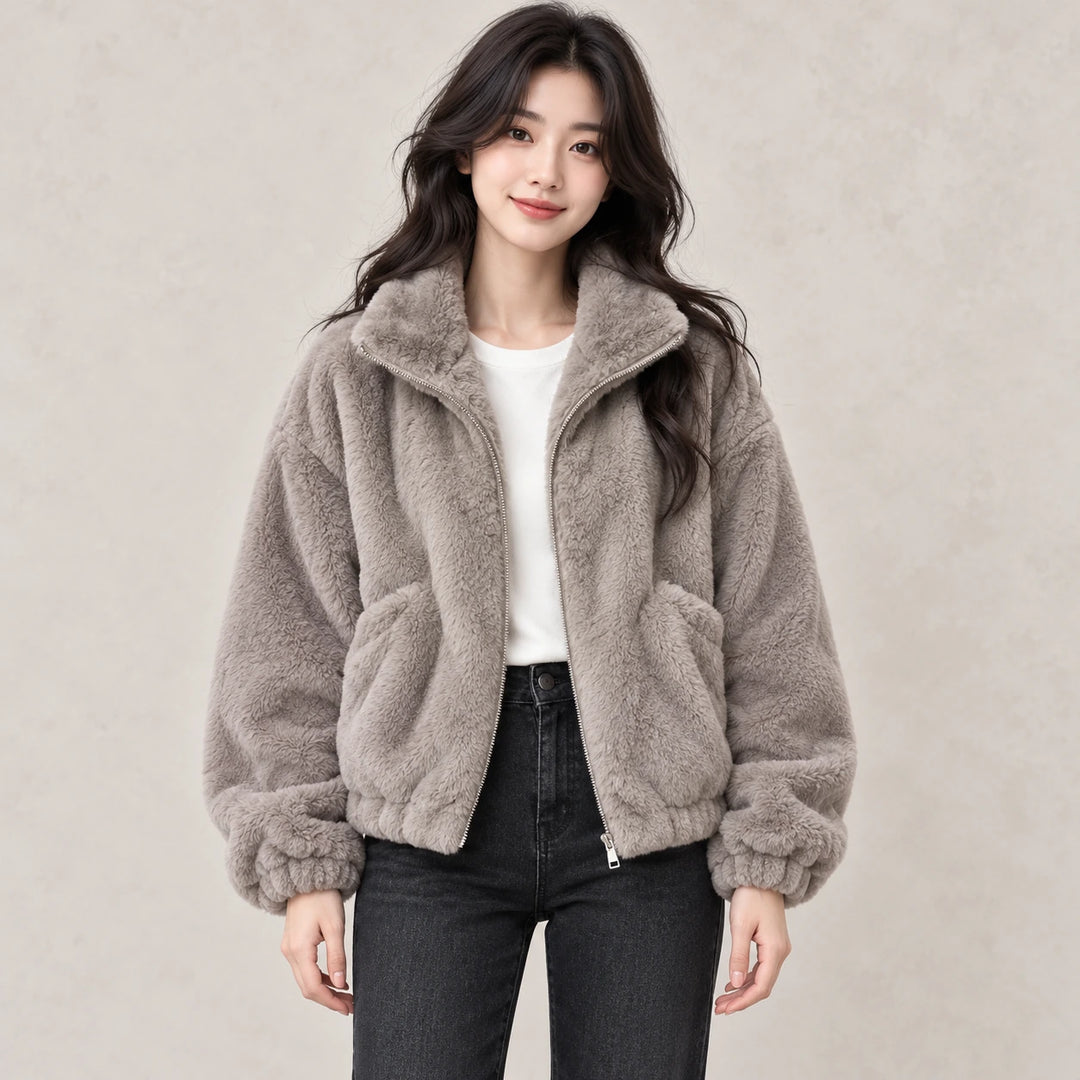 Model wearing a gray plush jacket with a white top and dark jeans, showing the front zipper, collar, cuffs and patch pockets.