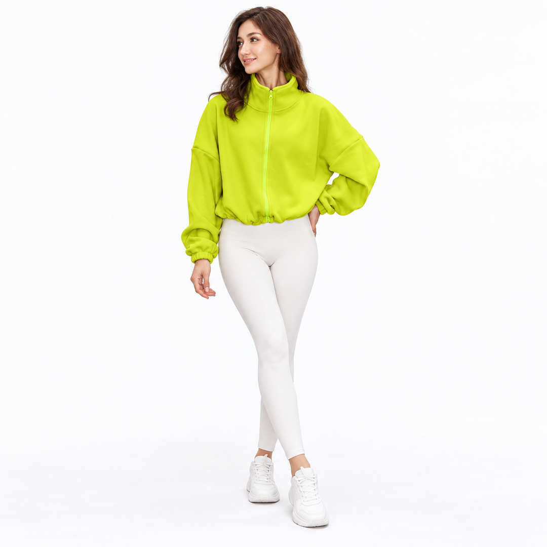 Neon yellow cropped jacket on a full-body model in a three-quarter pose, showing front zip, loose sleeves and gathered cuffs.
