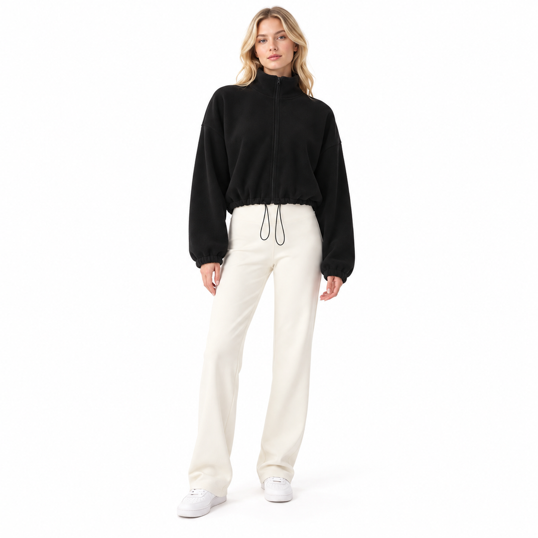 Black cropped jacket on a standing blonde model with stand collar, front zipper and hem drawcord, styled with ivory trousers.