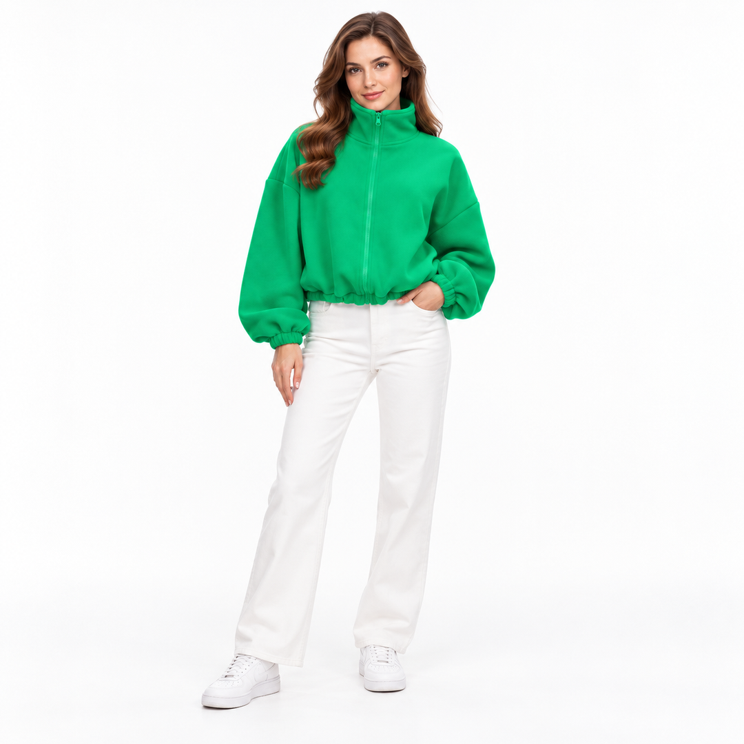 Emerald green cropped jacket on a full-body brunette model, showing stand collar, zipper, gathered cuffs, and white trousers.