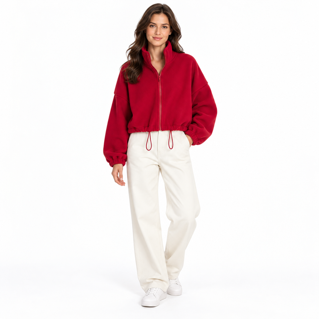 Deep red cropped jacket on a full-body brunette model, showing a stand collar, front zipper and drawcord with ivory trousers.