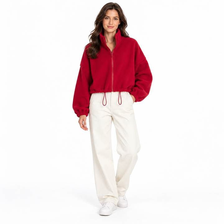 Deep red cropped jacket on a full-body brunette model, showing a stand collar, front zipper and drawcord with ivory trousers.