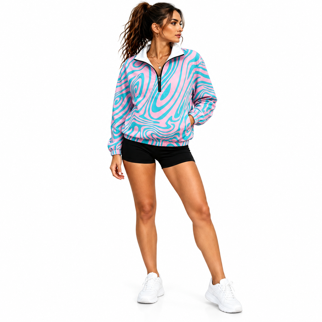 Side-angled view of a woman wearing a pink and cyan swirl pullover jacket, black shorts and white sneakers in a white studio.