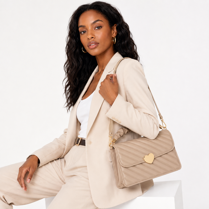 Warm beige quilted heart-clasp shoulder bag shown with a professional Black woman model in an elegant seated studio pose.
