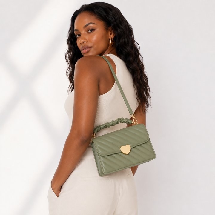 Sage green quilted heart-clasp shoulder bag worn by a professional Black woman model in a rear three-quarter studio view.