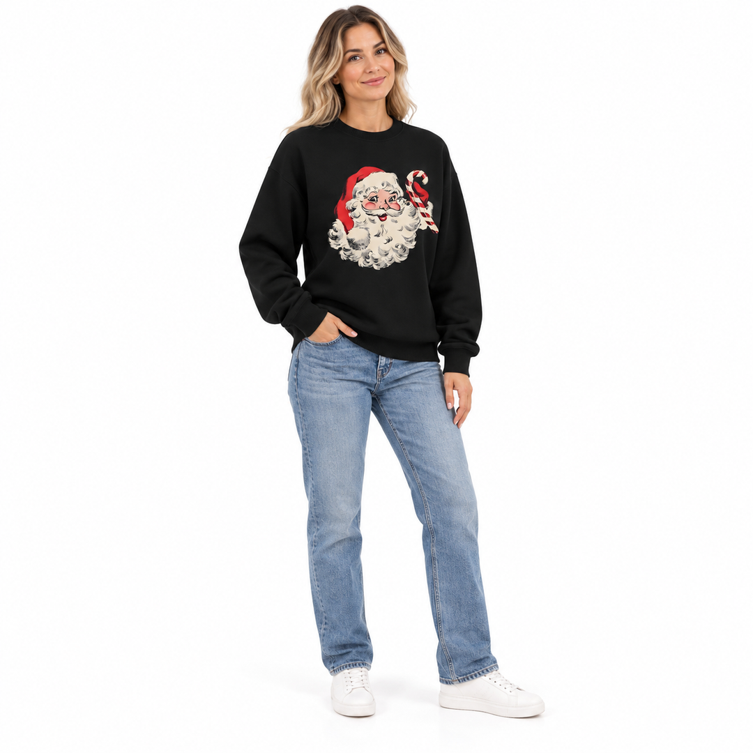 Woman modeling a black crewneck with Santa Claus and candy cane print, blue jeans and white sneakers against a white backdrop