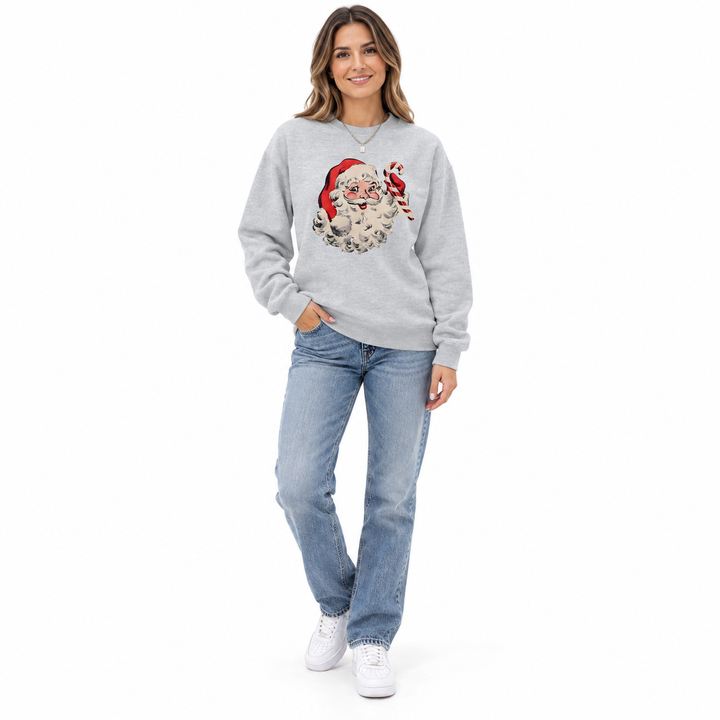 Full-length smiling woman wearing a gray crewneck with Santa Claus &amp; candy cane print, jeans and sneakers on a white backdrop