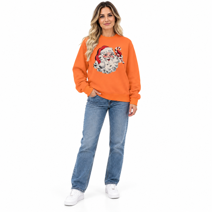 Woman wearing an orange crewneck with Santa Claus &amp; candy cane print, blue jeans and white sneakers against a white backdrop.