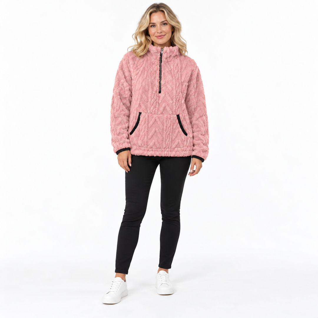 Pink textured zip front pullover on a full-body blonde model in black trousers and white sneakers, with the collar zipped up.