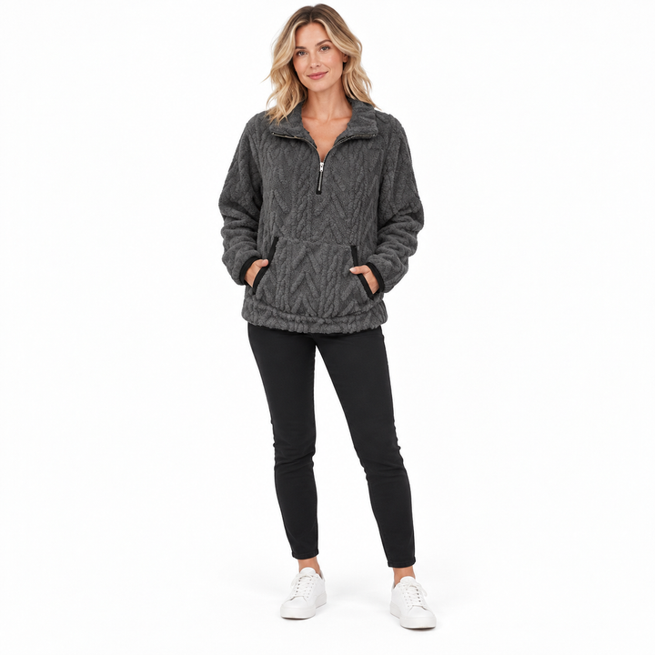 Dark gray textured zip-neck pullover on a blonde model with hands in front pockets, black trousers and white studio sneakers.