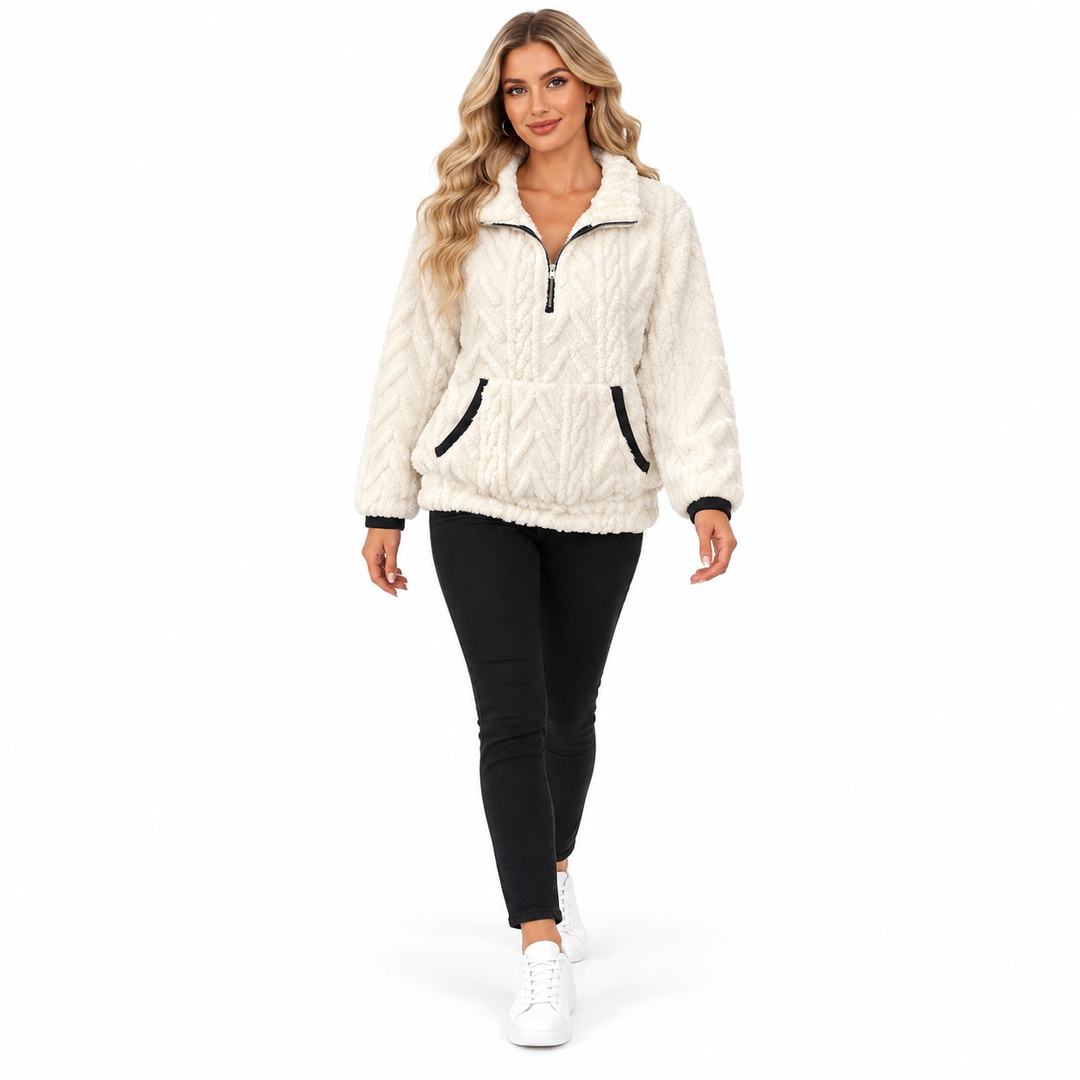 Blonde woman walking in a white textured pullover, black trousers and white sneakers against a seamless white studio setting.