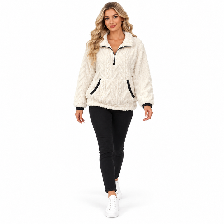 Blonde woman walking in a white textured pullover, black trousers and white sneakers against a seamless white studio setting.