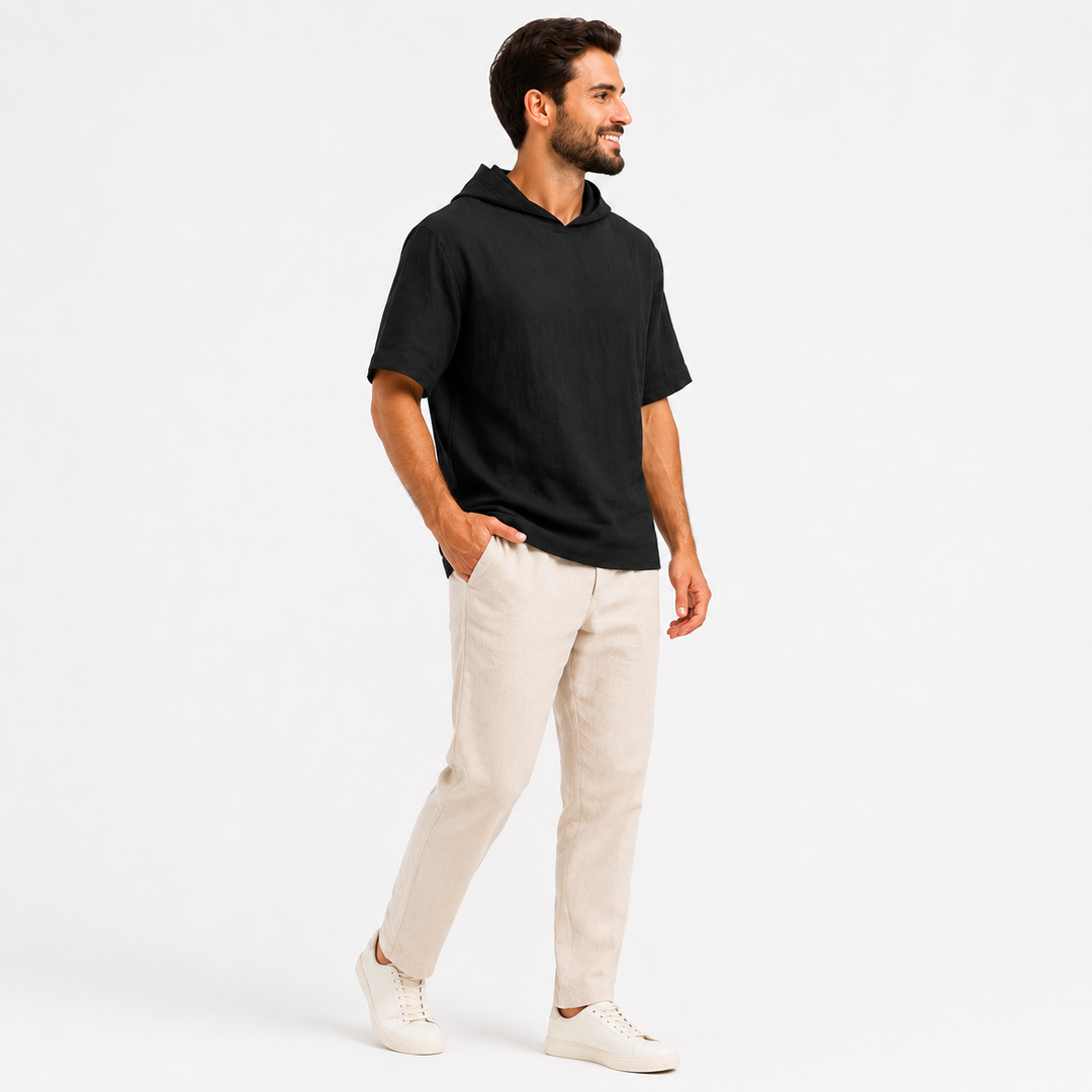 Man wearing a black short sleeve pullover hoodie, side view showing the sleeve and relaxed silhouette.
