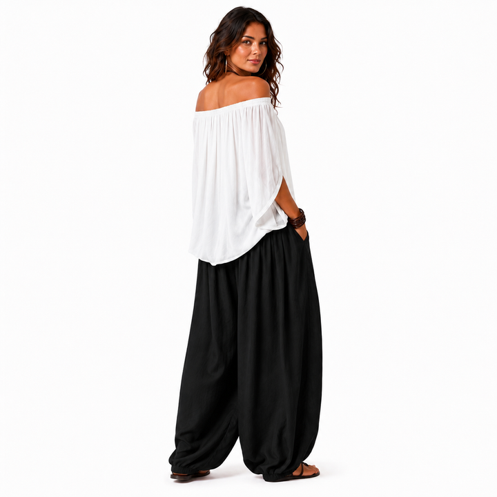 Woman in a white off-shoulder top and black gathered pants, rear three-quarter view showing the outfit drape.
