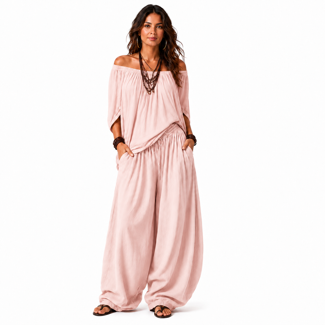 Woman wearing a blush pink off-shoulder top and matching gathered pants, full-body view on a white background.