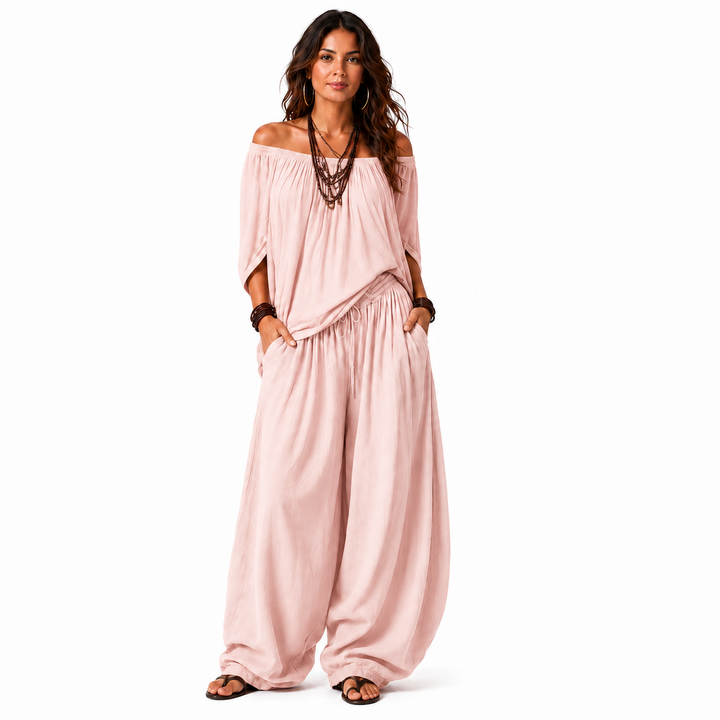 Woman wearing a blush pink off-shoulder top and matching gathered pants, full-body view on a white background.