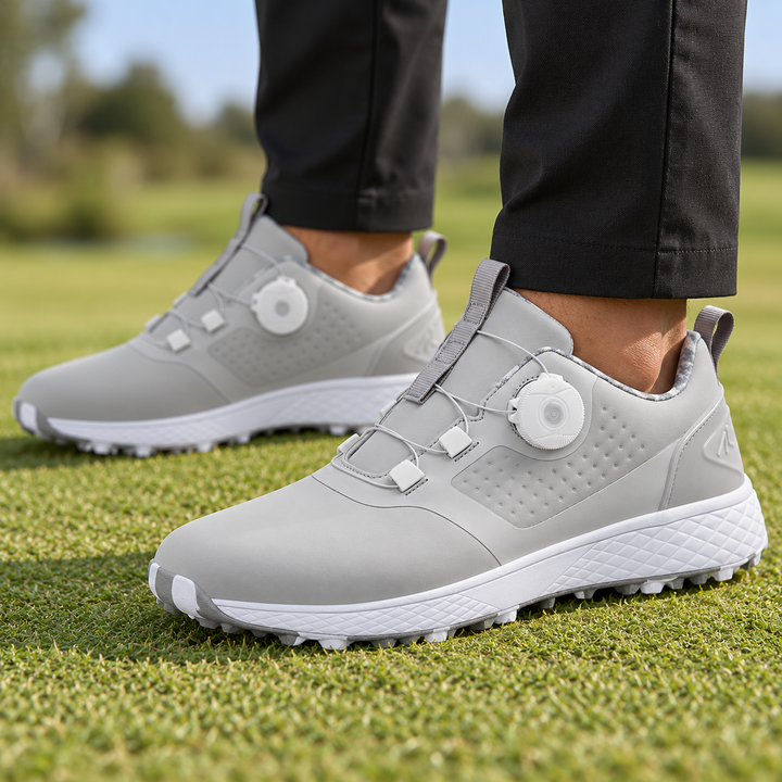 Gray rotary buckle shoes worn with black trousers on grass, showing the white side dial, cable fastening and textured midsole