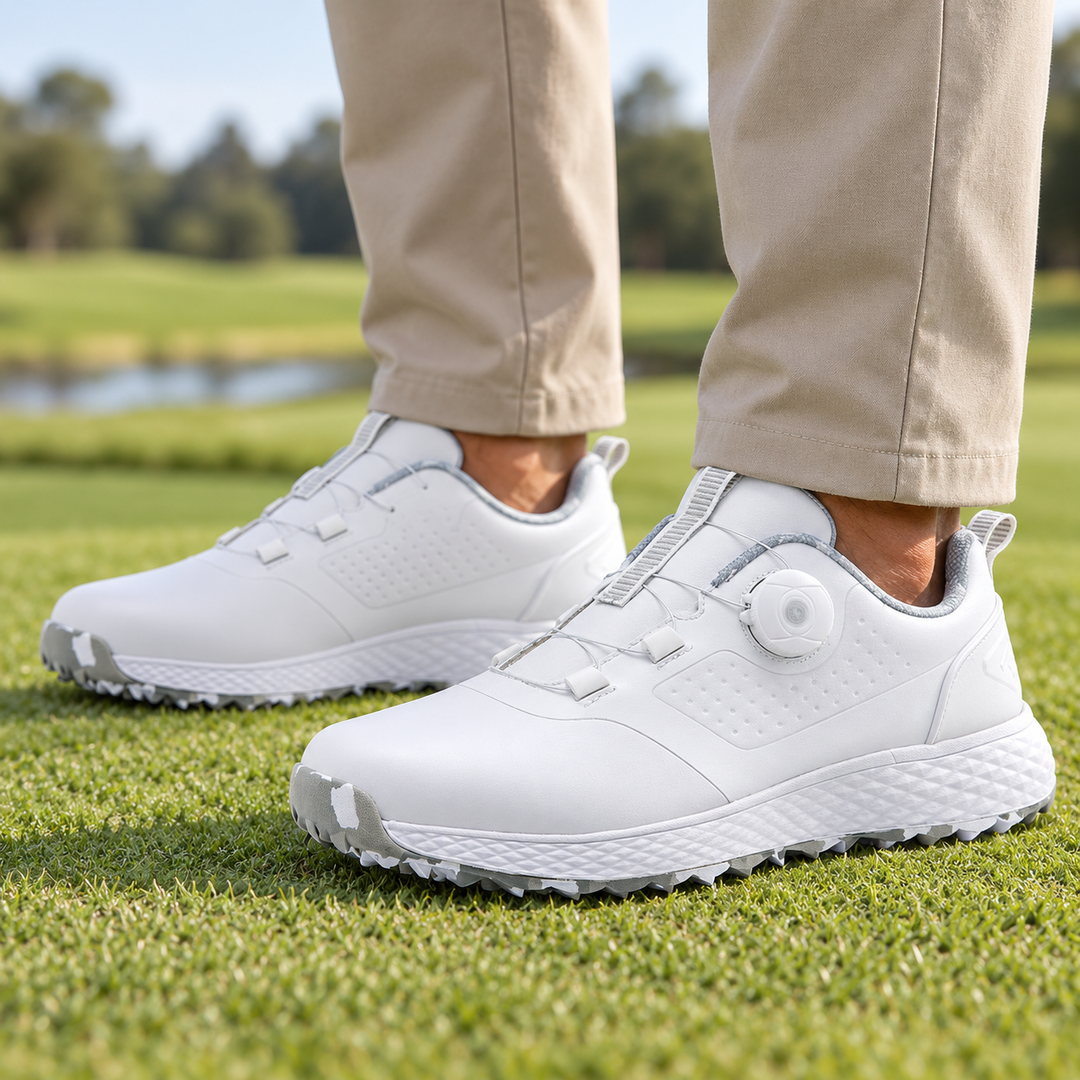 White and gray rotary buckle footwear worn with sand trousers on grass, showing the side dial, cable fastening and sole edge.