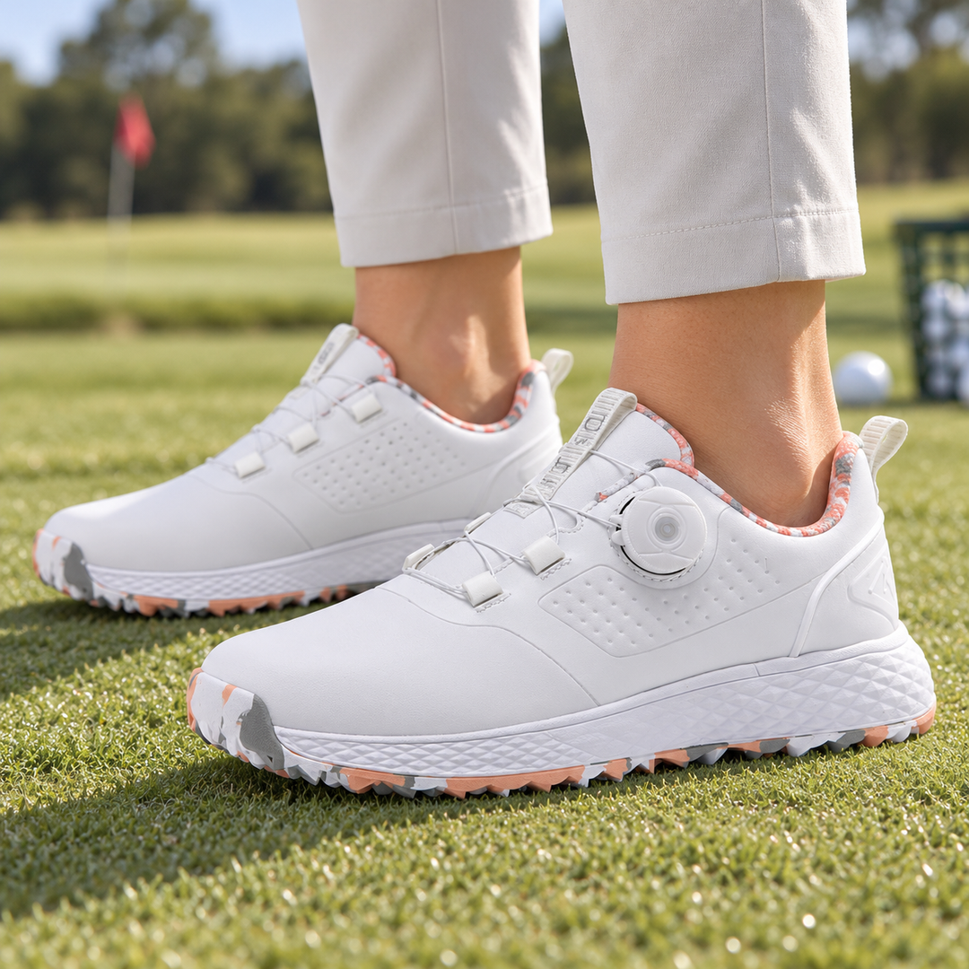 White and pink rotary buckle footwear worn with light trousers on short grass, with a white dial and patterned lining visible