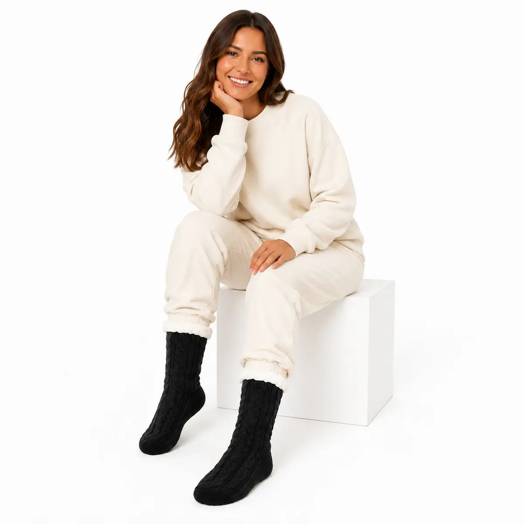 Black Style 2 cable knit lounge socks with plush cuffs modeled by a seated woman on a clean white studio background.
