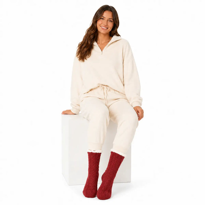 Red cable knit lounge socks with contrasting plush cuffs modeled by a seated woman on a clean white studio background.
