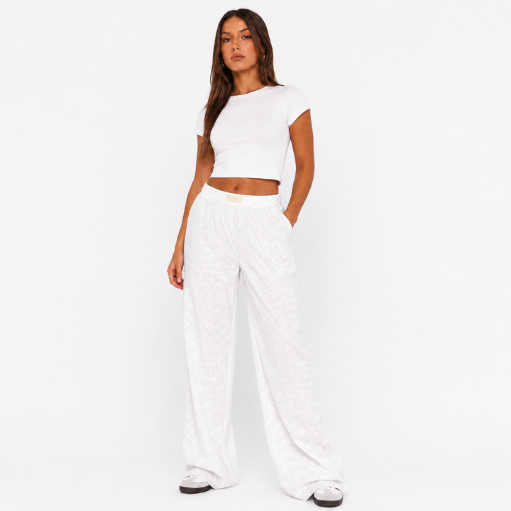 White wide leg pants for women on a studio model, showing elastic waist, textured fabric and relaxed full-length silhouette.