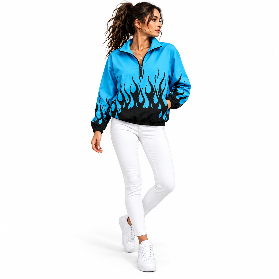 Woman wearing a blue and dark flame printed jacket with white jeans and white sneakers shown walking in a plain white studio.
