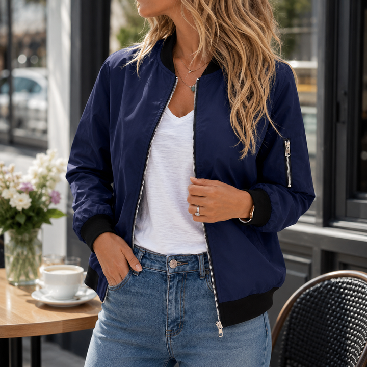 Navy zip-front bomber jacket styled with a white top and blue jeans in the cafe setting for relaxed everyday outfit layering.