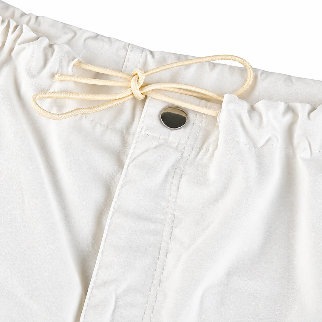 Close-up of white cargo pants at the waist, showing gathered waistband, drawstring bow, button fastening and front stitching.