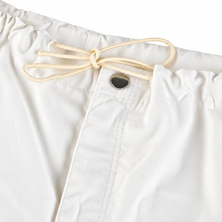 Close-up of white cargo pants at the waist, showing gathered waistband, drawstring bow, button fastening and front stitching.