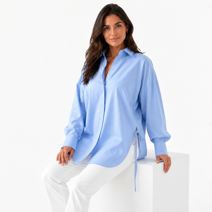 Woman seated in the powder blue long sleeve shirt with white trousers, highlighting relaxed drape and side tie.