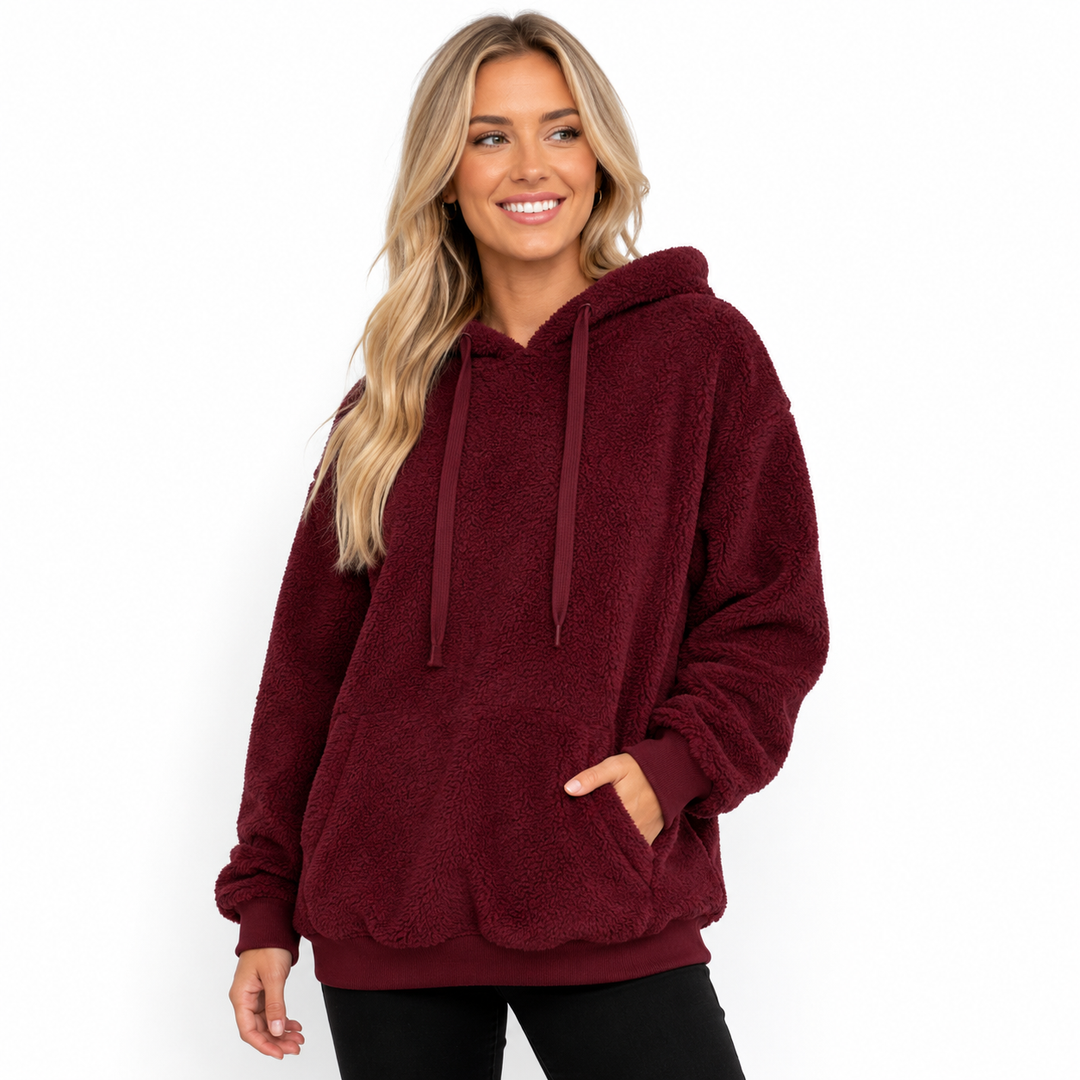 Burgundy hooded fleece pullover on a model with drawstrings, kangaroo pocket, cuffs and relaxed silhouette on white backdrop.