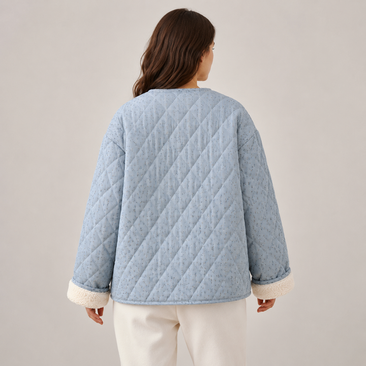 Back view of model in a blue floral quilted coat showing diagonal quilting, straight hem, long sleeves and cream lined cuffs.
