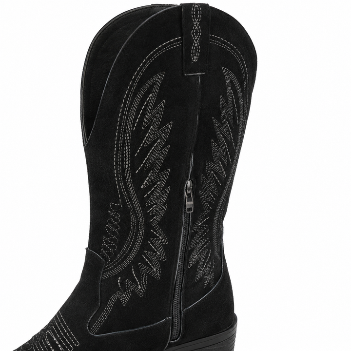 Black suede boot close-up showing the V-cut shaft, fine western embroidery, side zipper and visible surface texture on white.
